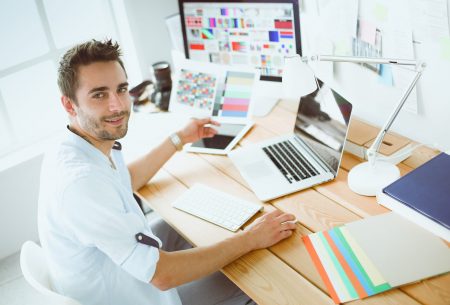 Portrait of young designer sitting at graphic studio in front of laptop and computer while working online