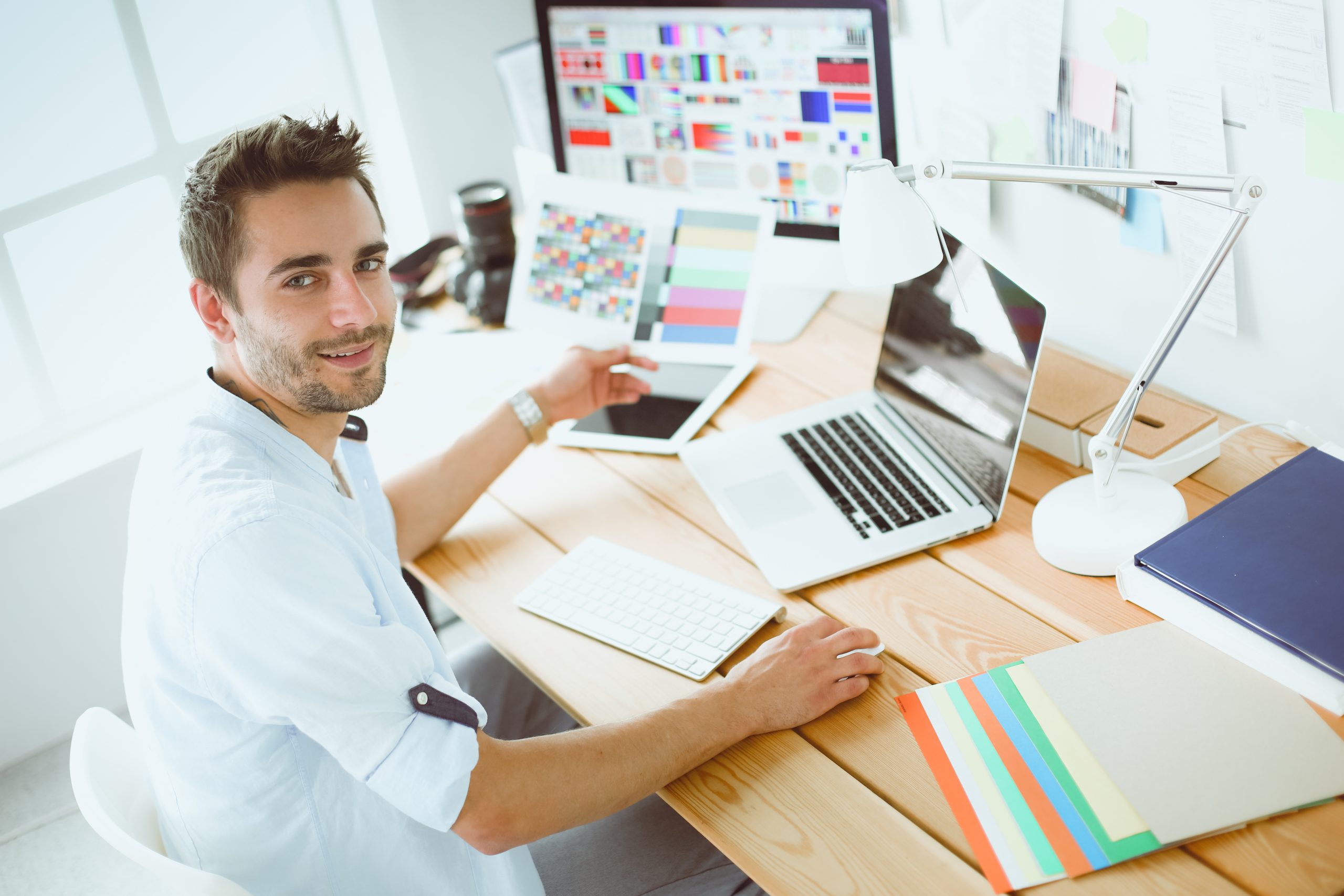 Portrait of young designer sitting at graphic studio in front of laptop and computer while working online.